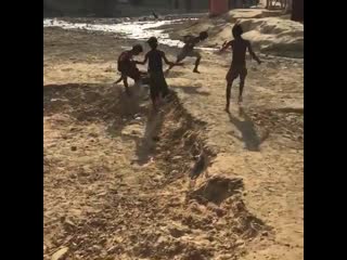 A group of porn playing football with a wooden crafted ball in a rough terrain in bangladesh