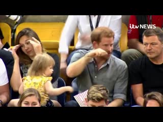 Mother realising her toddler is stealing popcorn from an unaware prince harry