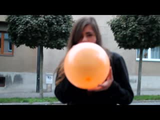 Czech girl blowing up a balloon until it pops outside