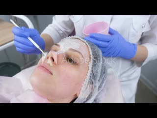 Beautician puts a white mask on the woman's face with a brush face close up