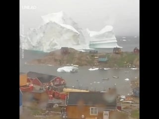 Just a huge 300 foot iceberg passing by a town in greenland