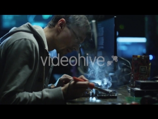 Softto electronics engineer is soldering an electric board with processors in office with display screens