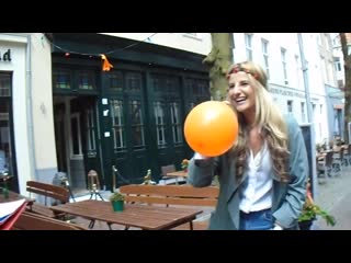 Girl blows up an orange balloon outside and someone stabs it