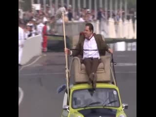 Mr bean riding atop a car with his royal scepter