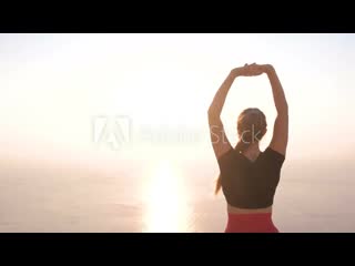 Beautiful view of woman doing yoga stretching on the mountain with sea view at sunset