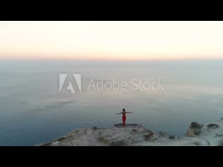 Woman is doing yoga meditation on the mountain with sea view at sunset back view